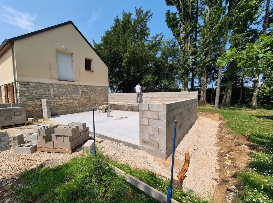 Chantier de construction extérieur en cours, un ouvrier debout sur une dalle béton fraîchement coulée