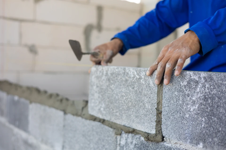 Chantier de construction en extérieur avec ouvrier en casque jaune et vêtements de travail bleus manipulant une benne à béton sur treillis métallique d'armature