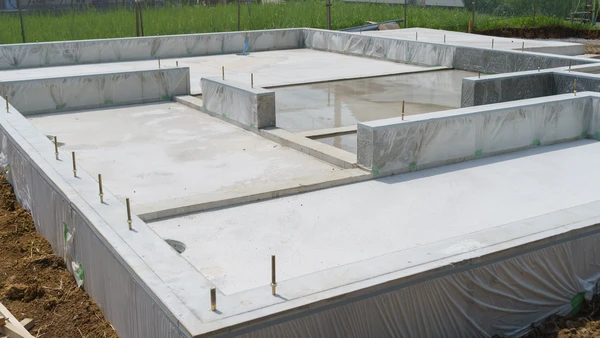 Ouvrier en bâtiment portant casque de chantier jaune et vêtements de travail blancs, assis sur établi en bois dans atelier