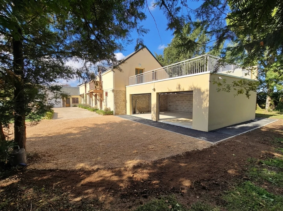 Propriété rénovée avec extension moderne en enduit jaune paille, garage double porte sectionnelle, terrasse en béton désactivé avec garde-corps métallique blanc
