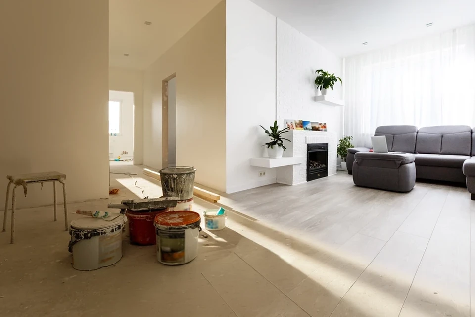 Personne peignant un mur intérieur, appliquant de la peinture blanche sur une surface grise avec un pinceau plat
